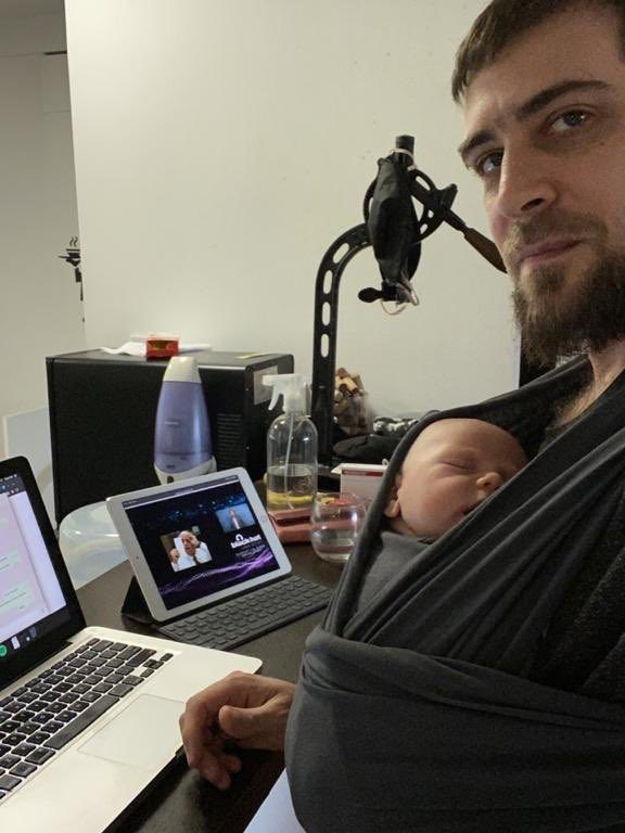 Un papá sentado frente a la compuadora, son su bebé en el fular.