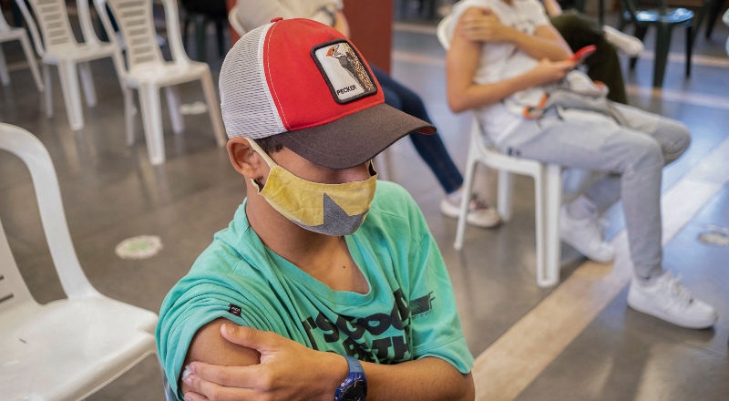 Chico con gorra se toma el brazo tras recibir vacuna.