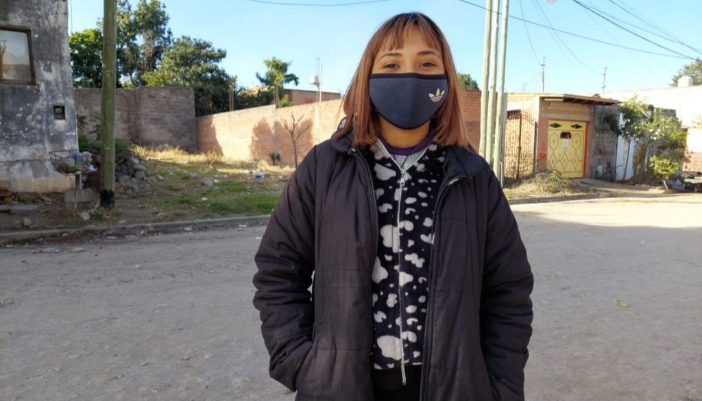 Una joven con barbijo, en un barrio de casas precarias.