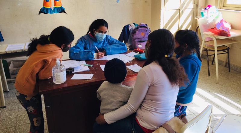 Una trabajadora de la salud escribe en su escritorio rodeada de adultos y niños de una comunidad rural de Santiago del Estero.