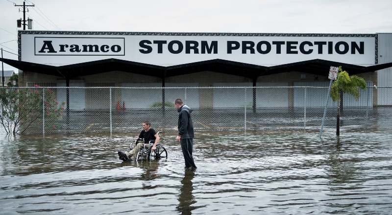 Una inundación en la que una persona en silla de ruedas intenta moverse, al lado de una persona que está parada y la observa.