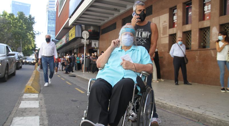 Una persona mayor en silla de ruedas llevada por otra persona más joven.