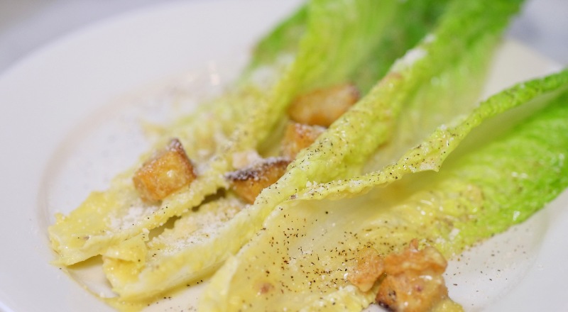 Una ensalada con tres tallos de lechuga y daditos de pollo.