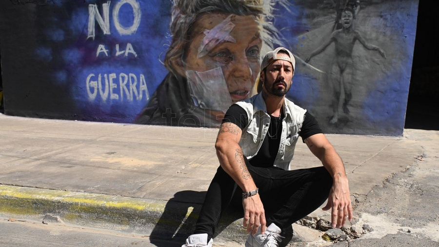 Maximiliano posa sentado delante de su mural.