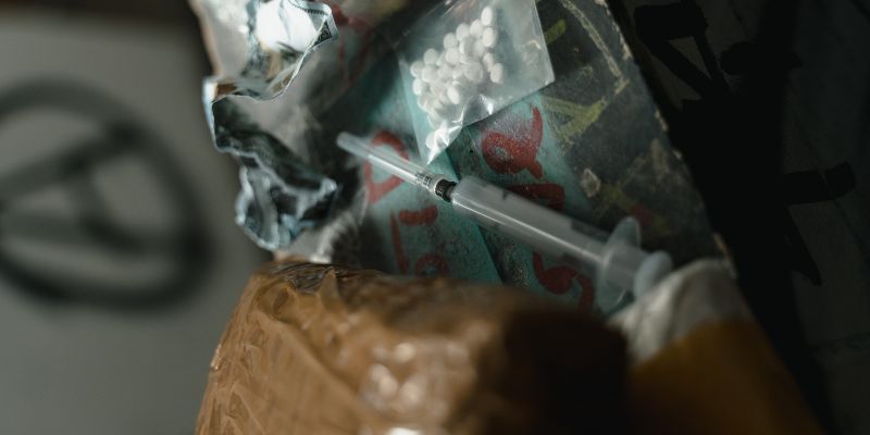Se observa un paquete de droga, pastillas y una jeringa usada.