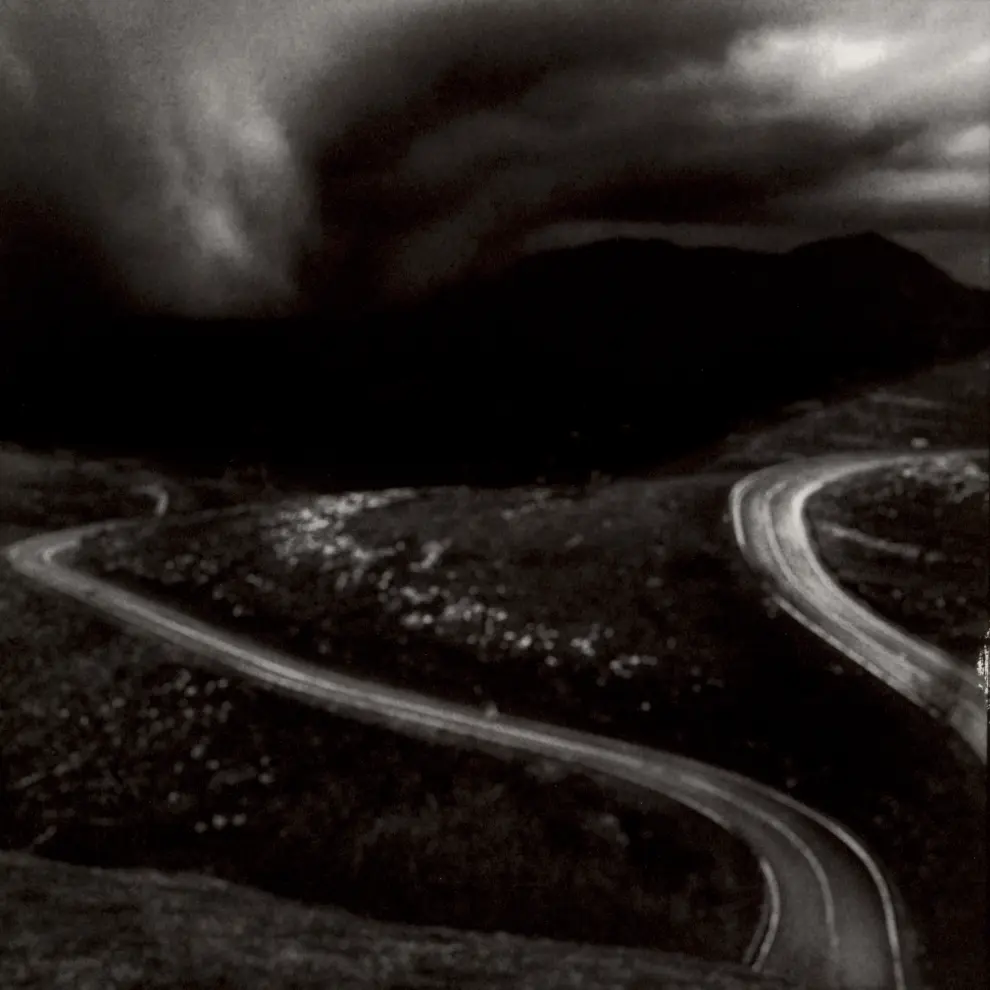 Una de las fotos de la muestra del fotógrafo Magano: Paisaje tomado desde un punto montañoso elevado, en el que se distinguen dos caminos de líneas curvas.